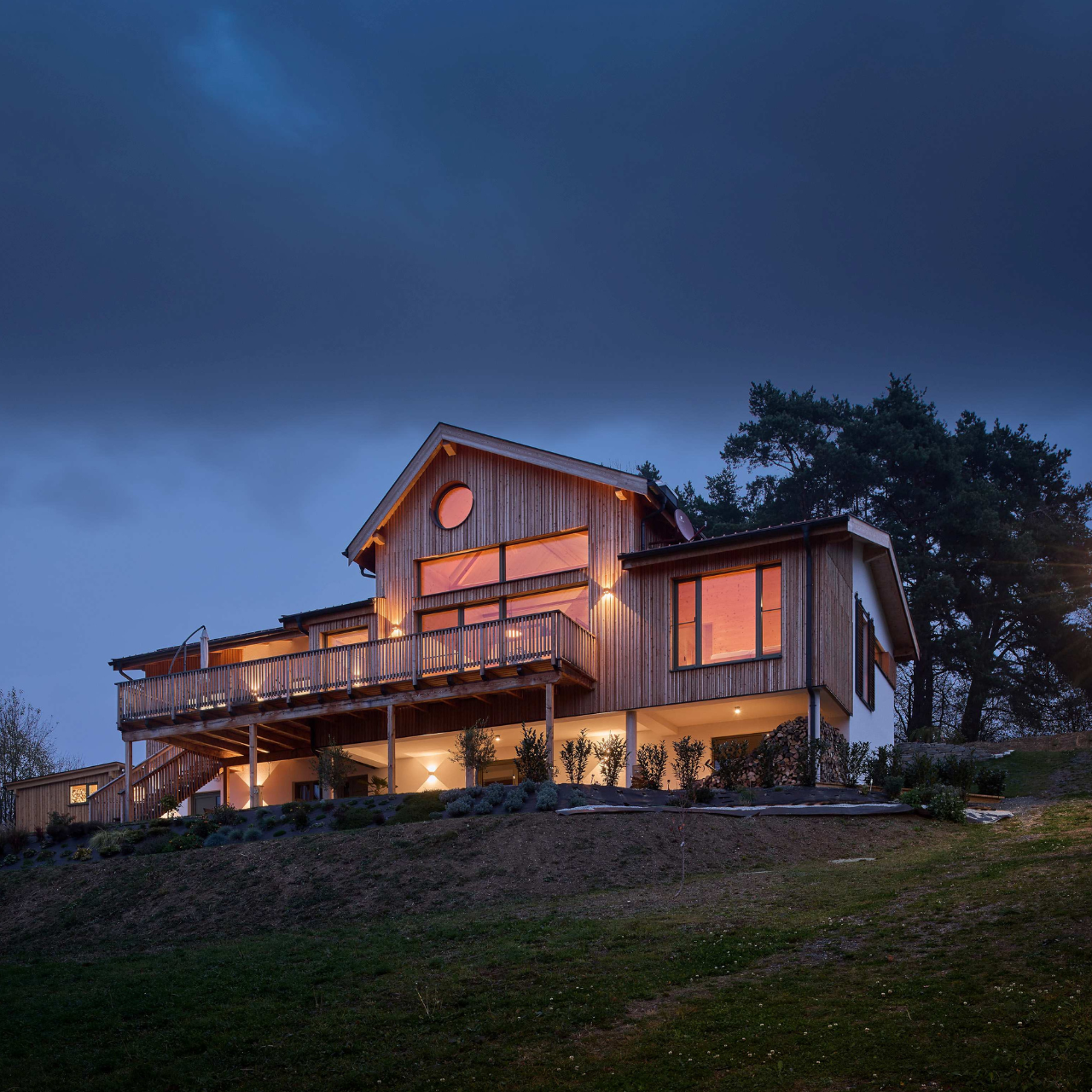 Ein Holz100-Haus aus mondgeschlagenem Holz bei Nacht. Es ist gemütlich beleuchtet.